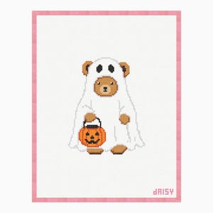 May include: A cross-stitch pattern featuring a brown bear wearing a white ghost costume with black eye holes. The bear holds an orange jack-o'-lantern bucket with a black handle. The design is on white fabric with a pink border and the word daisy.