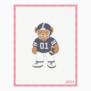 May include: A cross-stitch pattern featuring a brown teddy bear dressed as a football player in a navy blue jersey with the number 01, a navy helmet, and white pants, holding a brown football. The design includes a pink border and the text daisy.