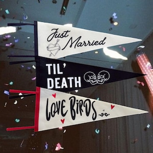 May include: Three pennant flags with wedding-themed messages. The top flag is white with black text that reads "Just Married" and a heart with an arrow. The middle flag is black with white text that reads "Til' Death" and two skull and crossbones. The bottom flag is white with red hearts and black text that reads "Love Birds".