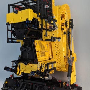 May include: A yellow and black Lego construction model of a large excavator with a detailed articulated arm and a black track system.