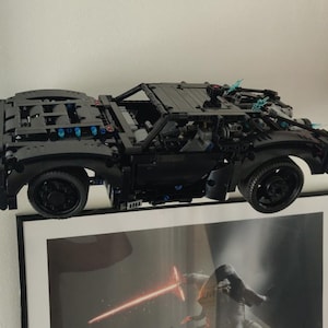 May include: A black Lego car model with blue accents, suspended in mid-air above a framed picture.