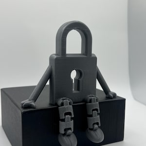 May include: A gray 3D printed padlock figurine with arms and legs. The padlock is sitting on a black box.