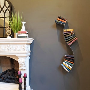 May include: A modern, wavy metal bookshelf with a variety of books on it. The bookshelf is mounted on a gray wall next to a white fireplace.