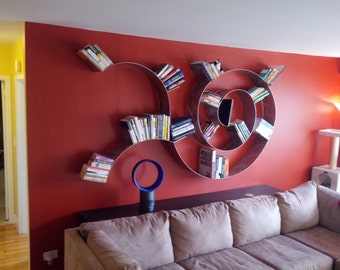 Peut inclure: Un mur rouge avec une bibliothèque unique en forme de cercles métalliques. La bibliothèque est remplie de livres et a la forme d'une spirale. Un canapé brun avec des coussins beiges est placé devant la bibliothèque.