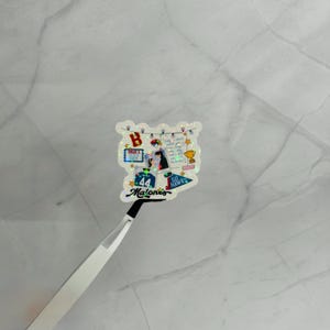 May include: A holographic sticker featuring a collage of images and text. The sticker includes a jersey with the number 44, the name "Malone's", and the words "Go Hawks". Other elements include a trophy and a letter "B".