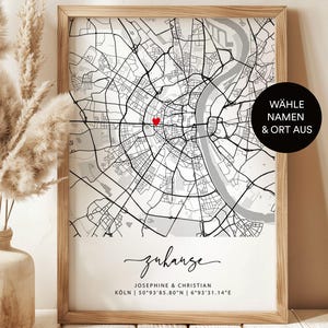 Könnte beinhalten: Eine schwarz-weiße Karte von Köln, Deutschland, mit einem roten Herzen, das einen Ort markiert. Der Text "Zuhause" ist in kursiver Schrift unter der Karte geschrieben. Der Text "JOSEPHINE & CHRISTIAN" und "KÖLN | 50°93'85.80"N 6°93′31.14"E" ist unter dem kursiv geschriebenen Text geschrieben. Der Text "WÄHLE NAMEN & ORT AUS" ist in einem Kreis in der oberen rechten Ecke der Karte geschrieben.