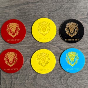 Könnte beinhalten: Sechs kreisförmige Untersetzer in Rot, Gelb, Schwarz und Blau, die jeweils ein goldenes Löwenkopf-Emblem und den darunter gedruckten Text FORGE HONOR aufweisen. Das Set enthält zwei rote, zwei gelbe, einen schwarzen und einen blauen Untersetzer.