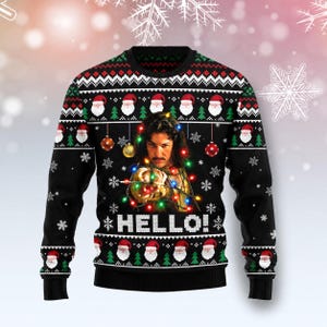 Puede incluir: Un suéter negro de manga larga y cuello redondo con un patrón repetitivo de caras de Papá Noel y pinos verdes. El centro muestra el retrato de un hombre con cabello oscuro y bigote, envuelto en luces navideñas, con el texto HELLO!