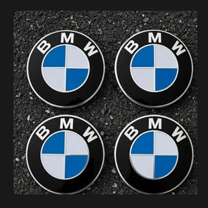 May include: Four black and silver BMW emblems with the BMW logo. The logo features a blue and white quadrant design, with the letters "BMW" in white at the top. The emblems are circular.