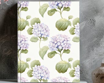 May include: A rectangular hardcover journal featuring a repeating pattern of light purple hydrangea blossoms and green leaves on a white background. The journal is positioned upright on a stack of two white books, displaying a floral botanical illustration.