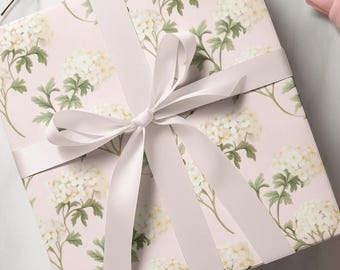 Peut inclure: Une boîte cadeau rose avec un motif floral blanc et un ruban de satin blanc noué en un nœud.