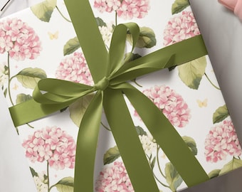 May include: A wrapped gift box featuring a floral pattern of pink hydrangeas and green leaves on a white background. The box is tied with a wide, olive green satin ribbon, forming a large bow.