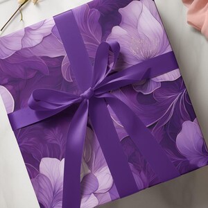May include: A square gift box wrapped in floral patterned paper with shades of purple and white. A matching purple satin ribbon is tied in a bow on top, creating a visually appealing presentation.
