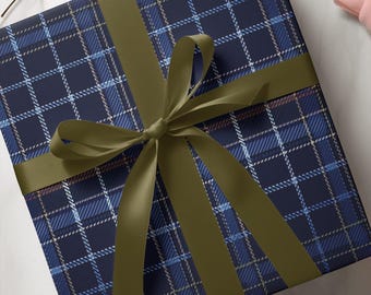 May include: A square gift box wrapped in dark blue paper featuring a plaid pattern of light blue and white intersecting lines. The box is tied with a smooth, olive green satin ribbon that is knotted into a decorative bow at the center.