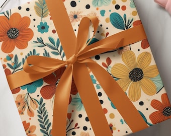 May include: A square gift box wrapped in cream-coloured paper featuring a repeating pattern of orange, yellow, and teal flowers, green leaves, and small black dots. The box is tied with a smooth, solid orange ribbon arranged in a cross pattern.