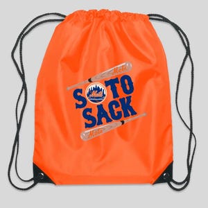 May include: Orange drawstring bag with a baseball-themed design featuring the text "Soto Sack" and the New York Mets logo. The bag has black drawstrings.