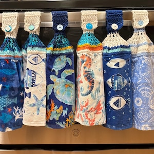 May include: Set of six crocheted dish towels with a nautical theme. Each towel features a different sea creature, including a seahorse, turtle, and fish. The towels are white with blue, orange, and green accents.