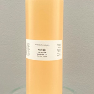 May include: A clear glass bottle with a white cap filled with a light yellow liquid. The bottle has a white label with the text "Georgia-Herbal.com" and "NEROLI 100% Pure Essential Oil Net Wt. 240ml."