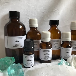 May include: A collection of six amber glass bottles with white labels containing essential oils. The bottles are of varying sizes and are arranged on a white surface with blue and green glass stones.