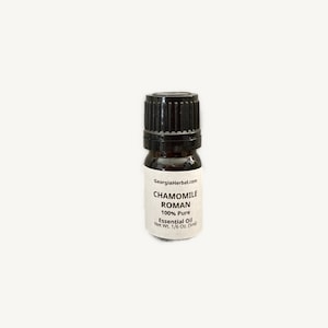 May include: A small, dark brown glass bottle with a black cap. The bottle is labeled "Chamomile Roman 100% Pure Essential Oil Net Wt. 1/6 Oz. (5ml)" and "georgiaherbal.com".