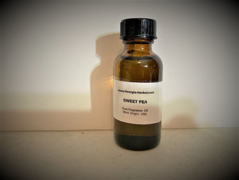 May include: A small brown glass bottle with a black lid, containing a clear liquid. The label reads "www.Georgia-Herbal.com SWEET PEA Pure Fragrance Oil 30ml Origin: USA".