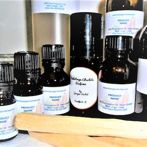May include: A collection of small glass bottles with labels that say "Product Name" and "100% Pure Essential Oil Steam Distilled". The bottles are arranged on a wooden surface with a wooden stick.