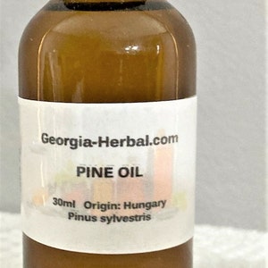 May include: A brown glass bottle with a black lid, labeled "Georgia-Herbal.com PINE OIL 30ml Origin: Hungary Pinus sylvestris".