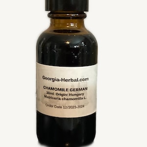 May include: A brown glass bottle with a black cap, labeled "Chamomile German" from Georgia-Herbal.com. The label indicates a 30ml volume and origin in Hungary. The bottle contains a dark liquid.