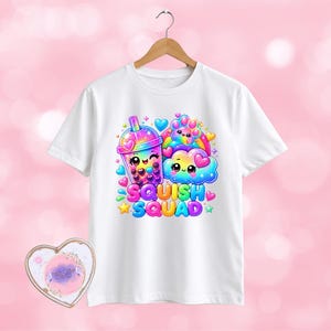 May include: A white short-sleeved t-shirt featuring a colourful graphic of a boba tea cup, a cloud, and a paw print with smiling faces. The text SQUISH SQUAD is printed in bold, multi-coloured bubble letters below the illustrations, surrounded by hearts and stars.