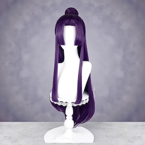 Op de afbeelding: Een lange, donkerpaarse pruik met een knot en pony, tentoongesteld op een witte mannequinhoofd. De pruik heeft lange, rechte lokken en een kanten rand aan de basis. De achtergrond is een zacht, gedempt grijs.