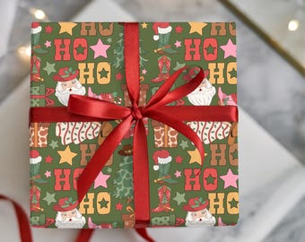 May include: A wrapped gift with a red ribbon. The wrapping paper has a green background with a repeating pattern of Santa Claus, cowboy boots, stars, and the word "HO" in a retro font. The bow is a deep red.