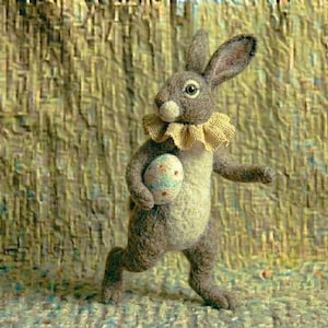 May include: A felt rabbit figure, with a cream body and grey fur, holding a speckled egg. The rabbit wears a ruffled collar. The background has a textured, woven appearance. A charming Easter decoration.