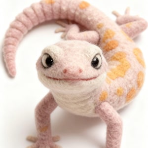 May include: A handcrafted felt gecko in pink and cream, with orange spots. The gecko has large, dark eyes and a smiling expression. The tail is curled, and the legs are outstretched, giving the impression of movement.