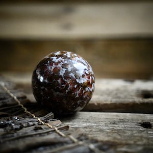 Può includere: Una sfera macchiata di marrone e bianco, che ricorda un piccolo pianeta, poggia su una superficie di legno invecchiato.