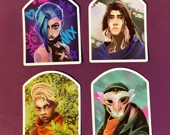 May include: Four stickers featuring character portraits. One has blue hair and the word "Jinx". Another shows a person with long brown hair. A third depicts a person with blonde hair and an orange scarf. The last shows a person wearing a white mask.