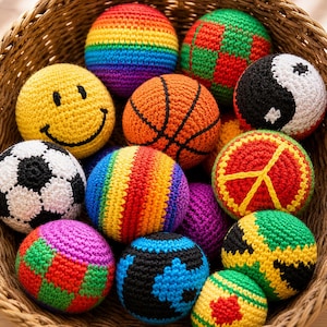 May include: A collection of colorful, crocheted balls in a woven basket. Designs include a smiley face, basketball, soccer ball, rainbow stripes, a yin-yang symbol, and a peace sign. The balls are various sizes and colors, creating a playful assortment.