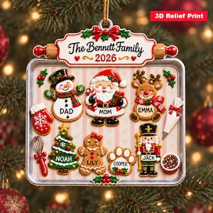 May include: A rectangular Christmas ornament shaped like a baking sheet with the text The Bennett Family 2026. It features 3D relief figures of a snowman, Santa, reindeer, tree, gingerbread person, paw print, and nutcracker with names.