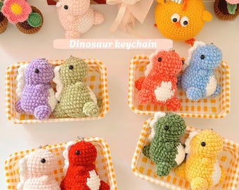 May include: A collection of colorful, crocheted dinosaur keychains in various colors, including pink, purple, green, red, blue, and yellow. Each dinosaur has a white belly and a spiky back. The text "Dinosaur keychain" is visible.