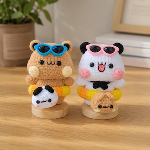May include: Two crocheted animal figures on wooden bases. The left figure is a tan bear with blue sunglasses and a yellow swim ring. The right figure is a white panda with pink sunglasses and a yellow swim ring. Both have small plush attachments.