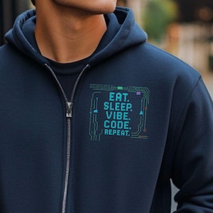 Op de afbeelding: Marineblauwe hoodie met ritssluiting en voorzakken. De tekst "EAT. SLEEP. VIBE. CODE. REPEAT." is in turquoise gedrukt in een printplaatontwerp op de borst. De ritssluiting is zilver.