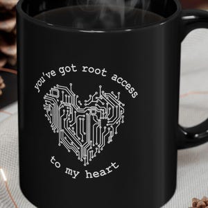 May include: A black ceramic mug featuring a white graphic of a heart formed by circuit board lines. The text "you've got root access to my heart" is printed in a circular pattern around the heart design. The mug has a handle on the right side.