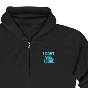May include: Black zip-up hoodie with a hood and front pockets. The hoodie features the text "I DON'T VIBE. I CODE." in light blue on the upper left chest. The hoodie has a full zipper closure and a drawstring hood.