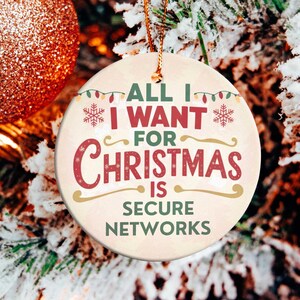 May include: A round Christmas ornament with the text "ALL I WANT FOR CHRISTMAS IS SECURE NETWORKS" in red and green. The ornament hangs on a snowy Christmas tree next to a glittery orange ball.
