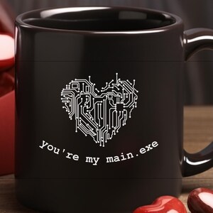 Op de afbeelding: Zwarte koffiemok met een wit hartontwerp van een printplaat en de tekst "you're my main.exe".