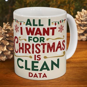 Peut inclure: Une tasse en céramique blanche avec le texte "ALL I WANT FOR CHRISTMAS IS CLEAN DATA" en rouge et vert. La tasse a une anse et est décorée de guirlandes lumineuses et de flocons de neige. La tasse est sur une surface en bois.
