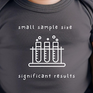 Könnte beinhalten: Ein dunkelgrauer Baby-Strampler mit weißem Text, der "small sample size" und "significant results" lautet. Zwischen dem Text befindet sich eine weiße Umrandung von drei Reagenzgläsern mit Blasen.