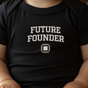 May include: A black baby bodysuit with the words "FUTURE FOUNDER" printed in white, along with a small white graphic of a microchip. The short-sleeved onesie is designed for infants and toddlers.