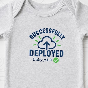 Puede incluir: Un body para bebé de color gris claro con mangas cortas que presenta un gráfico en azul oscuro y verde con un icono de nube, una flecha hacia arriba y el texto "SUCCESSFULLY DEPLOYED baby_v1.0" seguido de un icono de marca de verificación verde.