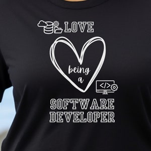 Könnte beinhalten: Schwarzes T-Shirt mit dem weißen Text "LOVE being a SOFTWARE DEVELOPER". Das Design beinhaltet ein Herz, ein Computerbildschirm-Symbol und ein Datenbank-Symbol. Das T-Shirt ist kurzärmelig.