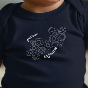 May include: Navy blue baby onesie with the words "precision engineered" and a graphic of interlocking gears in white. The onesie is made of soft material and is designed for comfort.